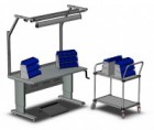 Pracovní stůl řady WB s osvětlením, podpěrou na nohy a stojanem na stohovací zásobníky. Na nastavitelném vozíku jsou umístěny další stojany na stohovací zásobníky pro zvýšení kapacity úložného prostoru.